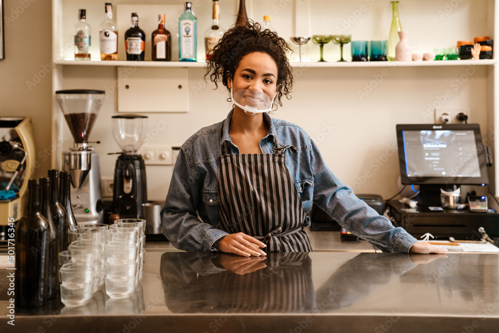 Black barista woman wearing face mask smiling while working in cafe Black barista woman wearing face mask smiling while working in cafe