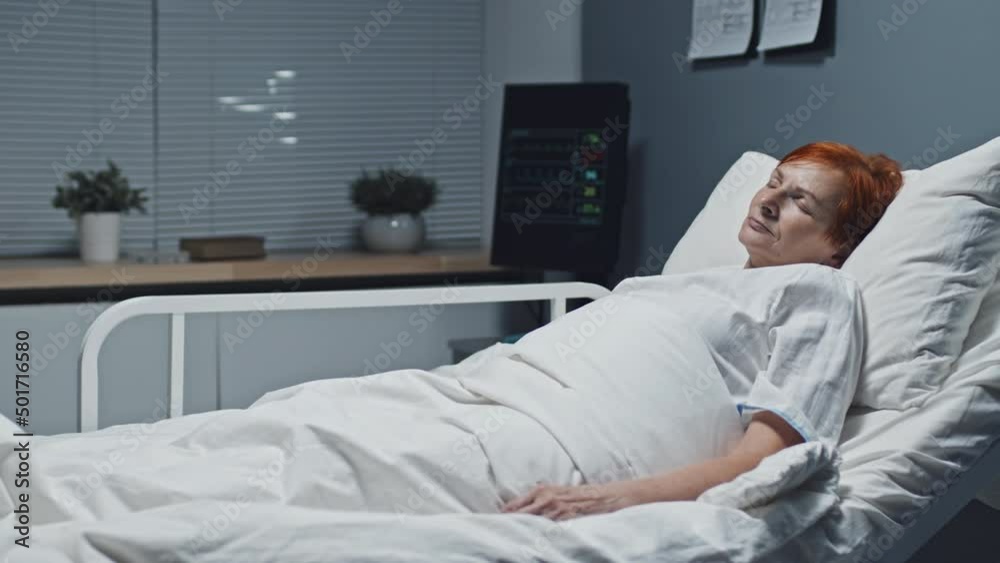 Medium long of older red-haired Caucasian woman sleeping in bed in clinic and smiling Medium long of older red-haired Caucasian woman sleeping in bed in clinic and smiling