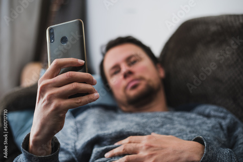 Young, handsome man lookiing at his smartphone at home on a couch