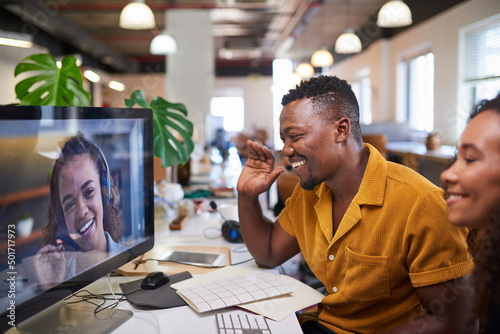 A Black man waves to his colleague on a video call from his office photo