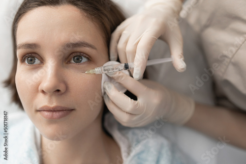 a cosmetologist doctor makes injections with a syringe with a small needle in the client s cheek. Facial wrinkle removal
