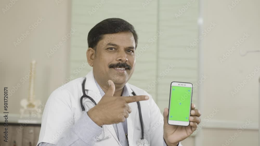 happy smiling doctor showing green screen mobile phone by pointing finger at hospital - conept of online consultation booking, app promotion and advertisement happy smiling doctor showing green screen mobile phone by pointing finger at hospital - conept of online consultation booking, app promotion and advertisement