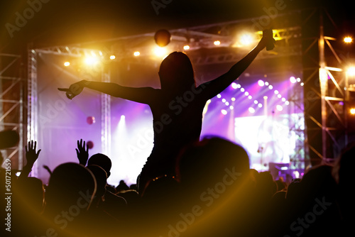 Girl silhouette with raising hands and mobile phone during enjoying music concert.