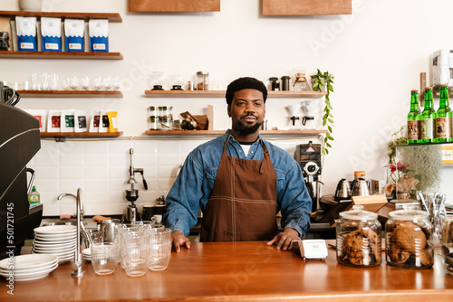 Black bearded man wearing apron smiling while working in cafe