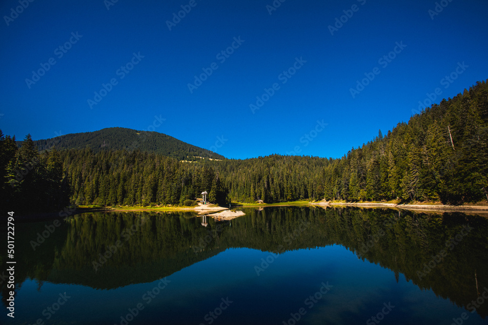 A clear lake against the backdrop of high green Carpathian mountains on a summer day