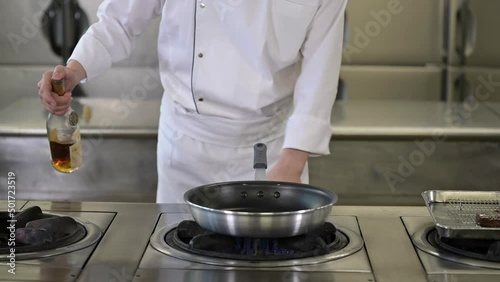 A chef in a white uniform creating a flambe with alcohol. Cooking pan catching fire. Flames in a kitchen. Slow motion footage.