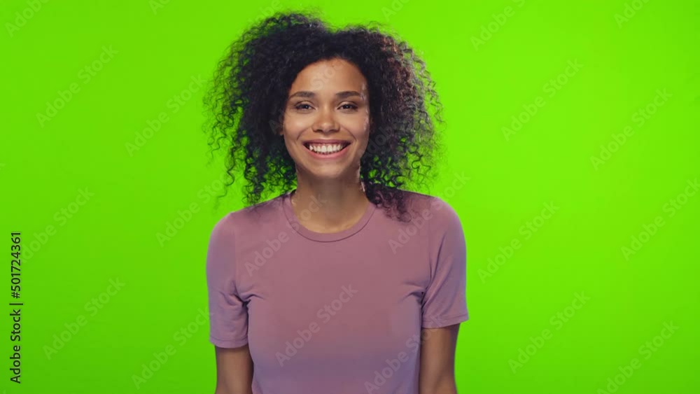 Young cheerful attractive African American woman student smiling and flirting covering eyes with hands playing oh who's here wearing casual t-shirt stands on studio green background. , Young cheerful attractive African American woman student smiling and flirting covering eyes with hands playing oh who's here wearing casual t-shirt stands on studio green background. ,