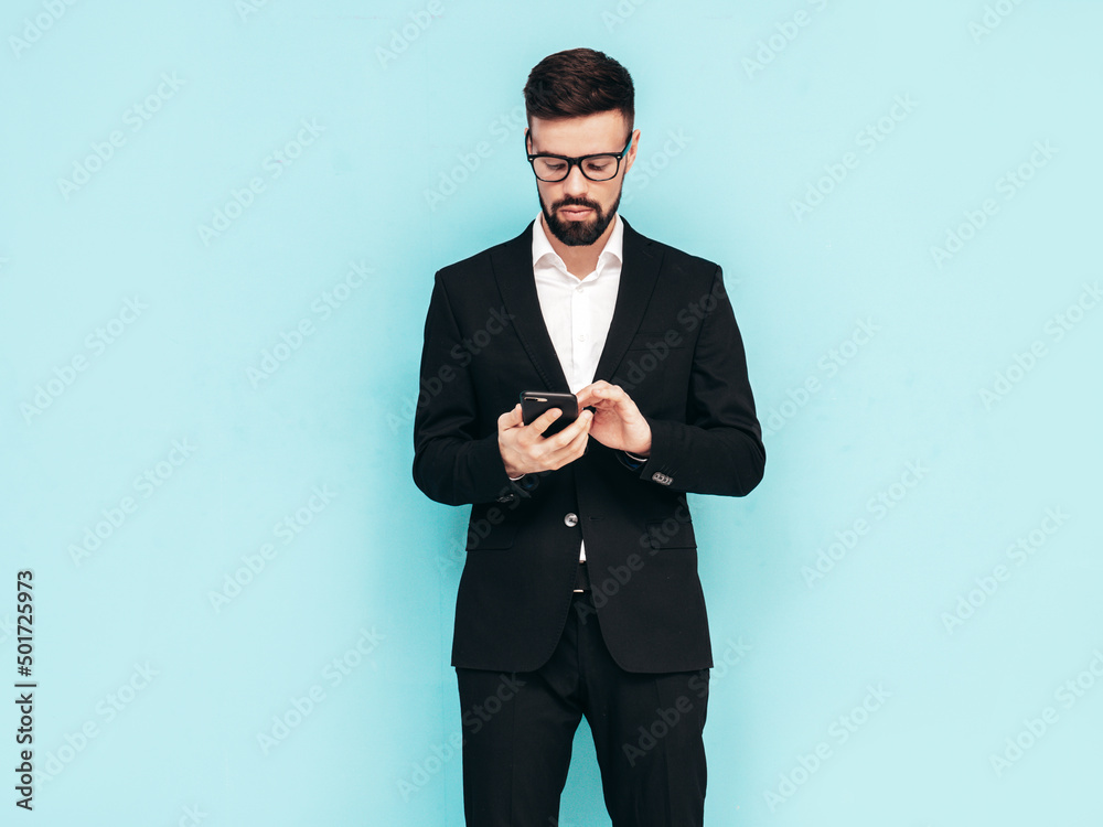 Handsome confident stylish hipster lambersexual model. Sexy modern man dressed in elegant black suit. Fashion male posing in studio. Holding smartphone. Looking at cellphone screen. Using apps Handsome confident stylish hipster lambersexual model. Sexy modern man dressed in elegant black suit. Fashion male posing in studio. Holding smartphone. Looking at cellphone screen. Using apps