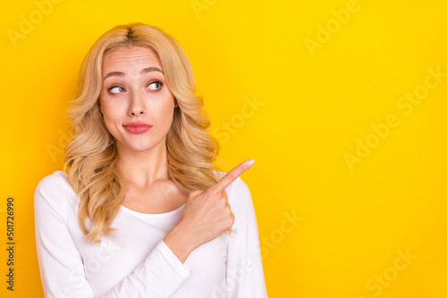 Photo of adorable doubtful lady dressed white shirt looking pointing empty space isolated yellow color background