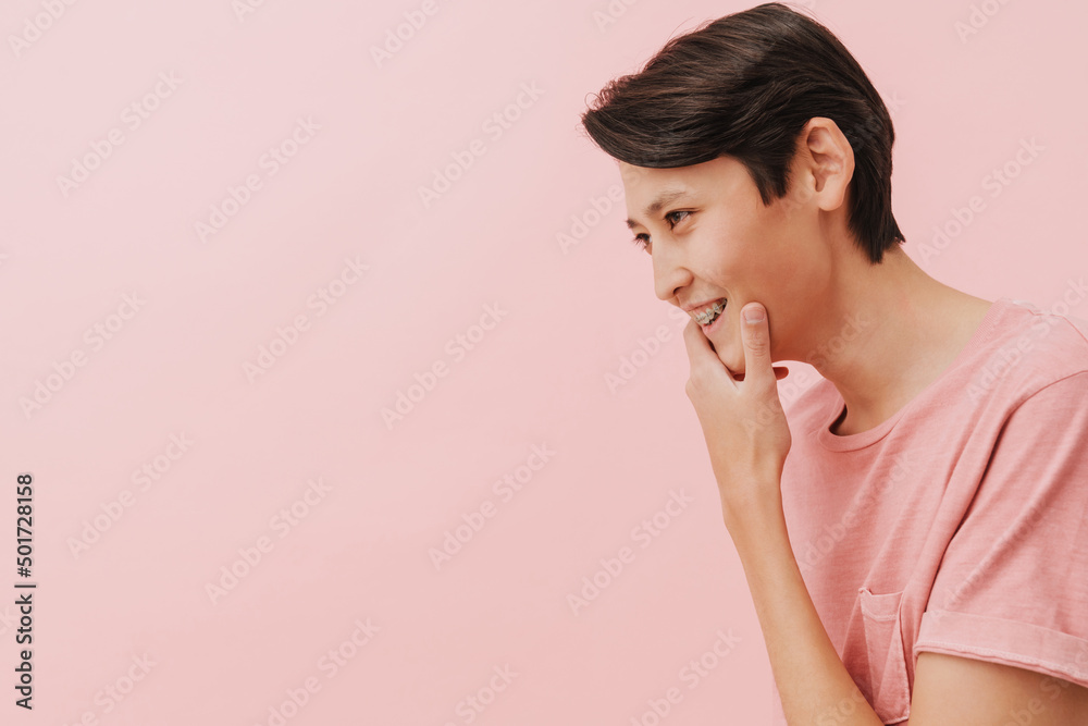 Asian brunette boy with dental brace smiling and looking aside Asian brunette boy with dental brace smiling and looking aside