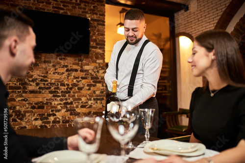 The waiter in uniform offers visitors wine in restaurant photo