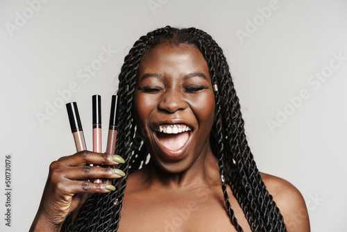 Shirtless black woman laughing while posing with lip glosses