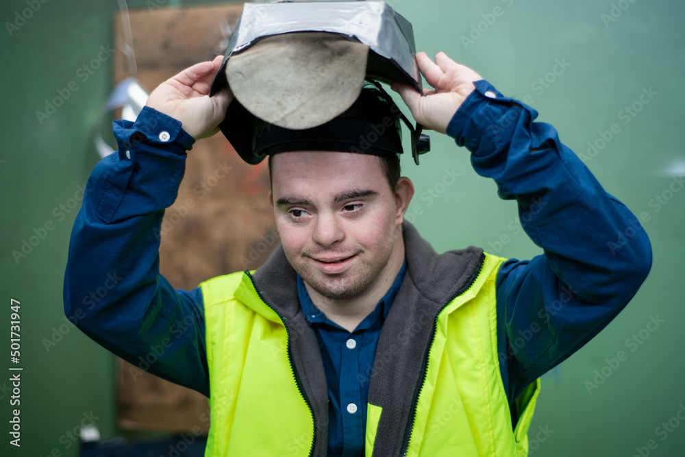 Young man welder with Down syndrome working in industrial factory, social integration concept.
