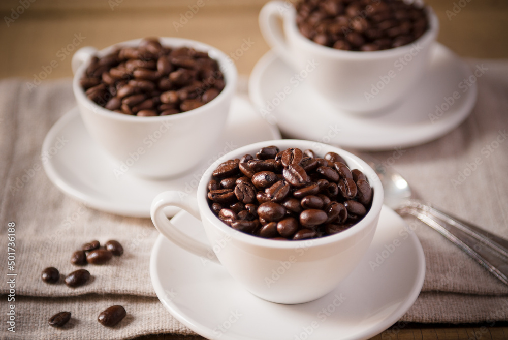 Three White Coffee Cups on White Saucers Filled with Coffee Beans Three White Coffee Cups on White Saucers Filled with Coffee Beans