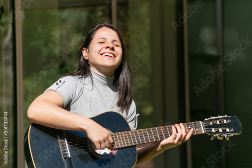 una mujer sonrriendo y tocando la guitarra en un dia soleado