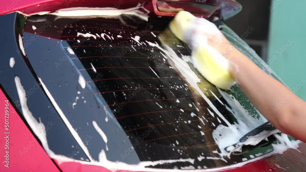 Closeup of a woman's hand washing a car with sponge and soap on the