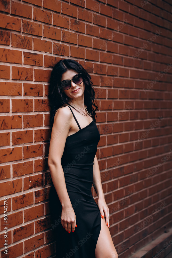 beautiful young slender girl in a black dress standing near a brick wall beautiful young slender girl in a black dress standing near a brick wall