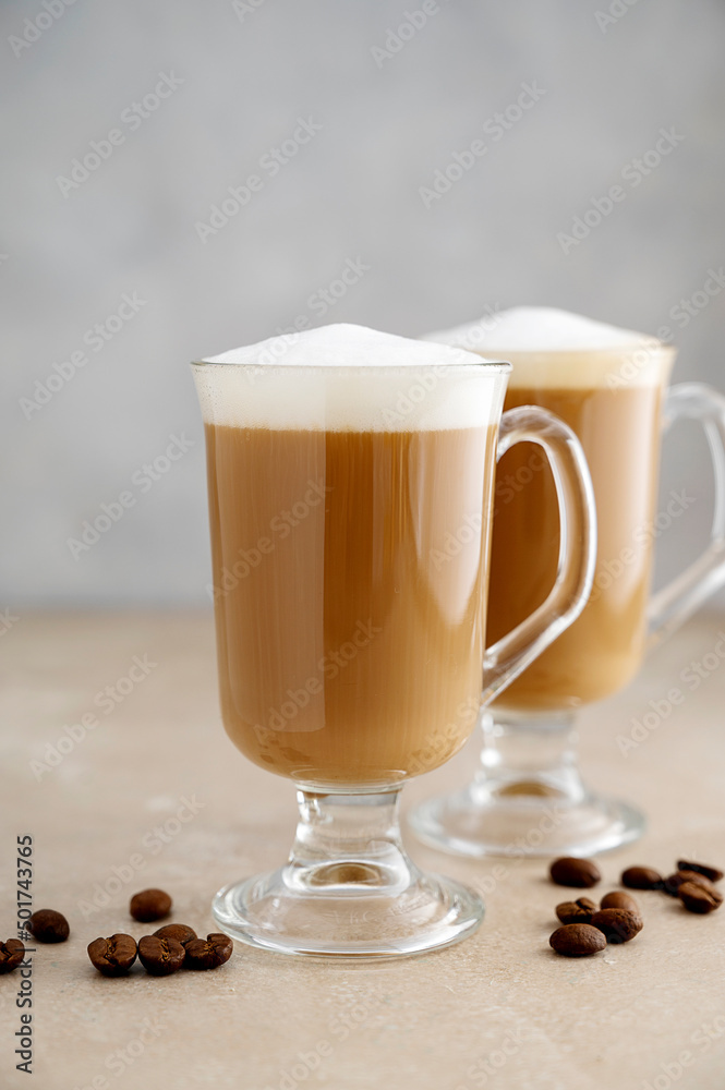 Coffee in glass ?ups with whipped milk foam on neutral background. Copy space for text. Coffee in glass ?ups with whipped milk foam on neutral background. Copy space for text.