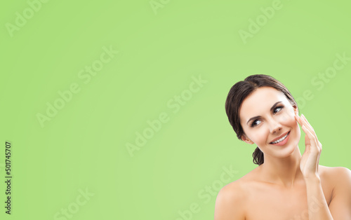 Portrait of beautiful dark haired woman cleaning face skin by cotton pad, isolated over green color background. Amazed smiling brunette girl at studio. Beauty model picture. Copy space empty text area