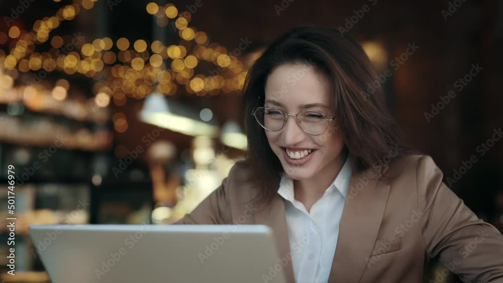 Charming caucasian woman smiling sincerely and waving with hand during video conference on wireless laptop. Business lady in eyeglasses sitting at cafe and talking with partners online. Charming caucasian woman smiling sincerely and waving with hand during video conference on wireless laptop. Business lady in eyeglasses sitting at cafe and talking with partners online.
