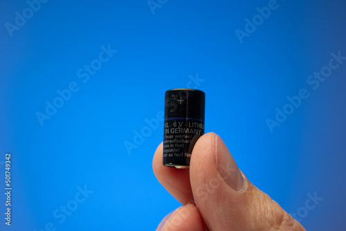 Small cylindrical PX28 Alcaline battery held between fingers by Caucasian male. Recycling concept, close up studio shot, isolated on blue background