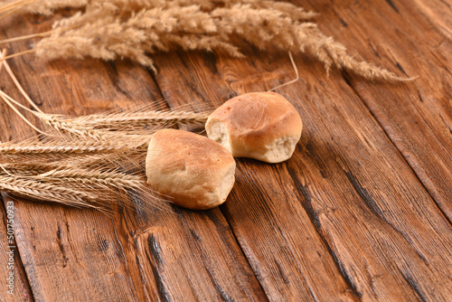 Freshly baked buns and ears of wheat on a wooden table.