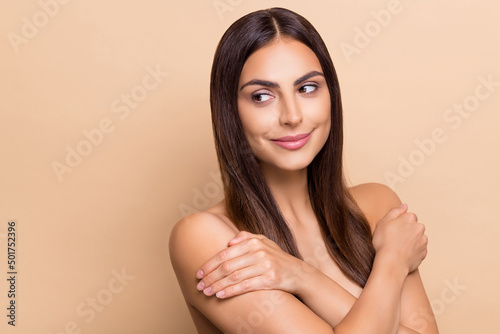 Portrait of attractive long-haired girl hugging shoulders looking aside copy space isolated over beige pastel color background