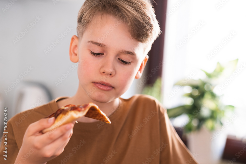 Teenager eats pizza while sitting in the kitchen at home. Quick lunch.