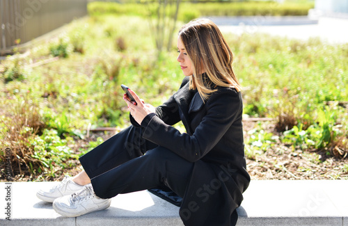 bellissima ragazza al parco che guarda il telefono e invia messaggi vocali photo