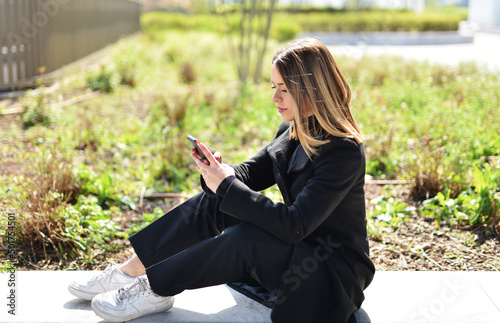 bellissima ragazza al parco che guarda il telefono e invia messaggi vocali photo