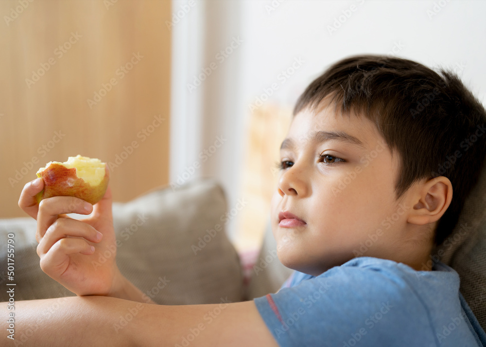 Healthy child eating red apple, Cute boy eating fresh fruit for his snack while watching TV in living room, Close up kid face eating food. Healthy food for children concept Healthy child eating red apple, Cute boy eating fresh fruit for his snack while watching TV in living room, Close up kid face eating food. Healthy food for children concept