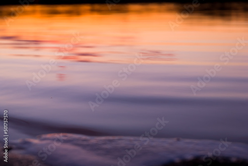 Orange, yellow and purple sunset on river with black trees reflection in water