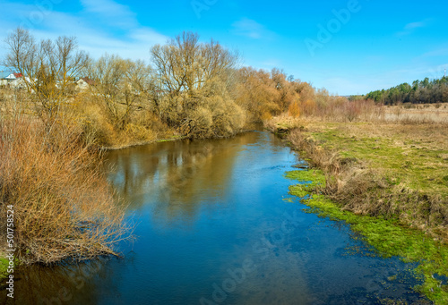 Beautiful colorful spring natural landscape with blue river surrounded by young tree leaves in sunlight