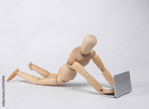 Wooden puppet uses laptop isolated on white background