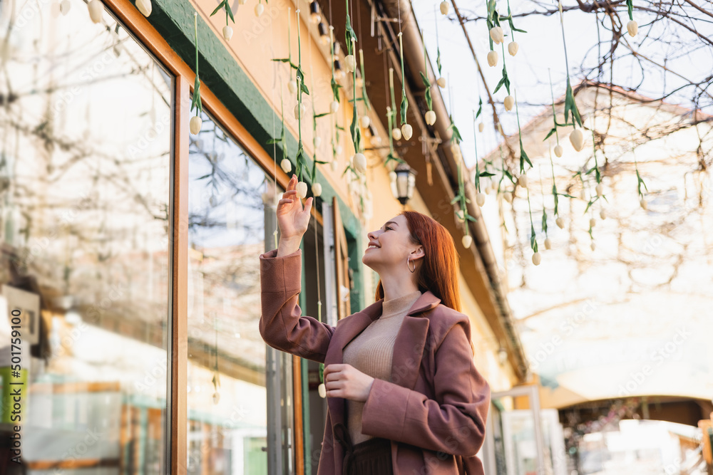 cheerful redhead woman in coat smiling while looking at hanging tulips outside. cheerful redhead woman in coat smiling while looking at hanging tulips outside.