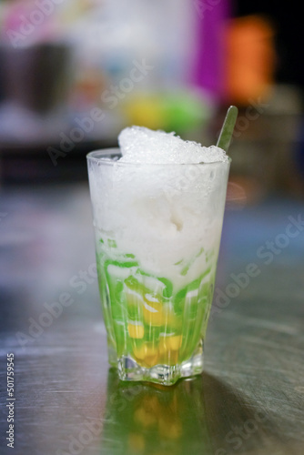 A cup of Lod Chong on the table with blurred background. It is a Thai dessert rice noodle eaten with coconut cream.
