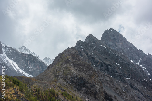 Atmospheric mountain landscape with large pointy pinnacle under gray cloudy sky. Gloomy scenery with high pointed mountain peak with sharp rocks in low clouds. Huge rocky peaked top in rainy weather. © Daniil