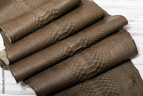 Brown khaki dyed folded natural genuine python leather on the wooden table 