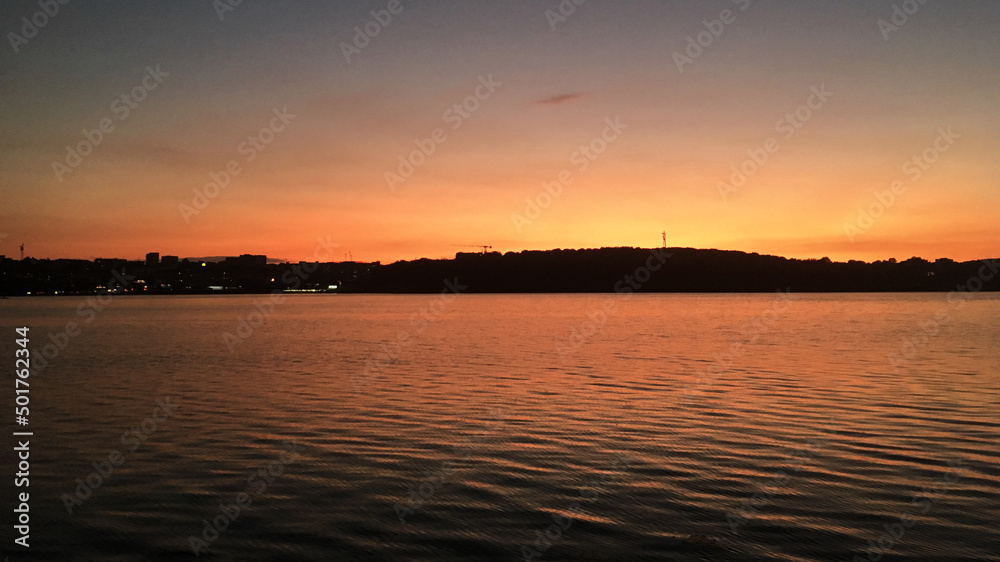 Beautiful sunset over lake Natural background with blue water and sky with yellow orange purple clouds, reflected in the lake. Breathtaking horizon panoramic view with setting sun.