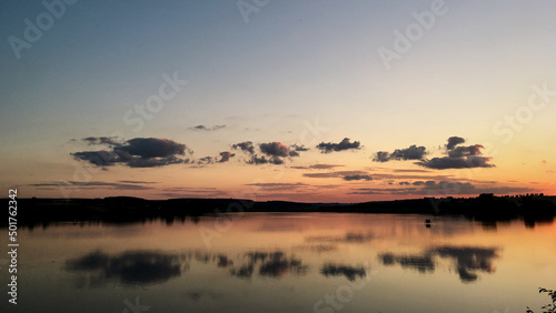 Beautiful sunset over lake Natural background with blue water and sky with yellow orange purple clouds  reflected in the lake. Breathtaking horizon panoramic view with setting sun.