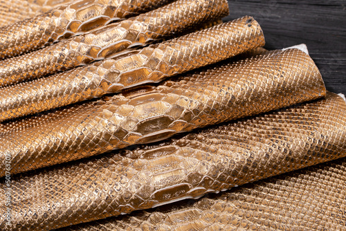 golden brown metallic dyed folded natural genuine python leather on the wooden table 