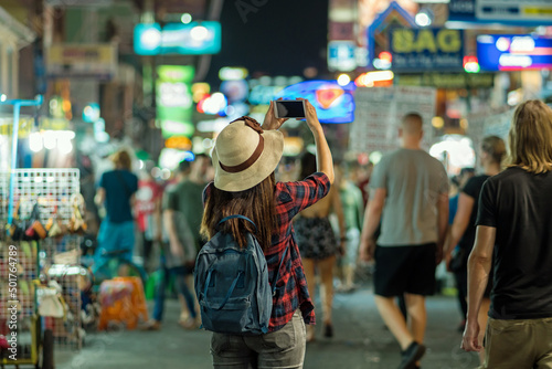 Back side of Young Asian traveling women taking photo in Khaosan Road walking street at night in Bangkok, Thailand, traveler and tourist concept photo