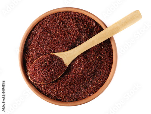 Ground sumac spice, pile in clay pot and wooden spoon isolated on white, top view  photo