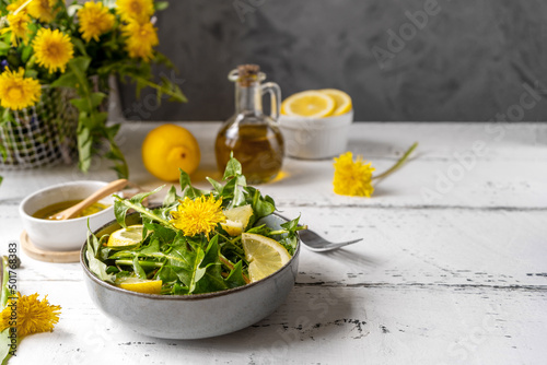Dandelion salad with olive oil, lemon juice and spices on white wooden table with grey background. Copy space