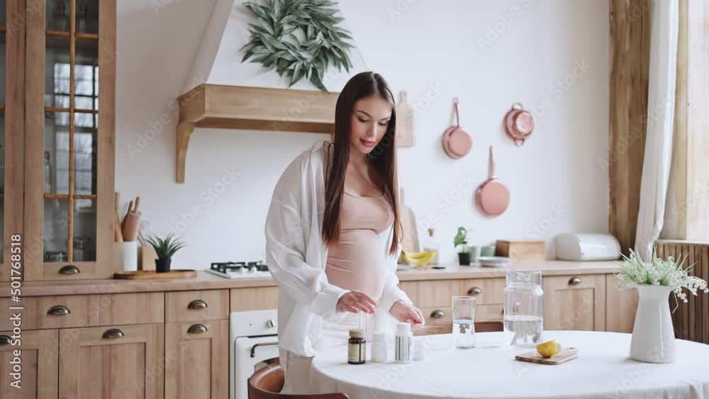 Pregnant woman takes bottles with vitamin pills at table Pregnant woman takes bottles with vitamin pills at table