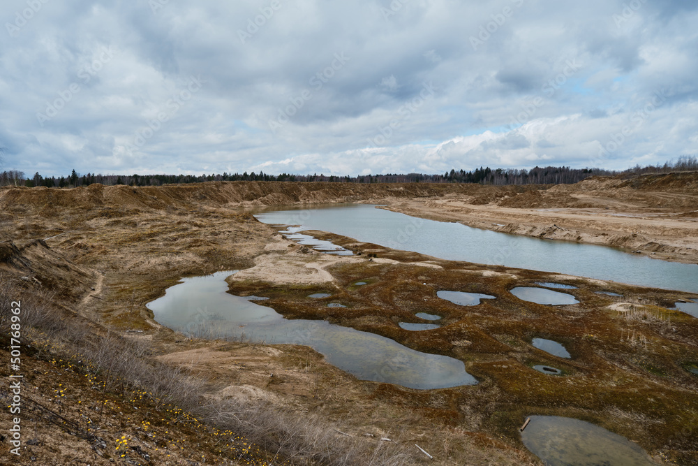 Artificially dug pits and ponds or lakes. Beautiful view of sand dunes and quarries with water in cloudy sunny weather in spring. Landscapes of Russia Moscow region. Artificially dug pits and ponds or lakes. Beautiful view of sand dunes and quarries with water in cloudy sunny weather in spring. Landscapes of Russia Moscow region.