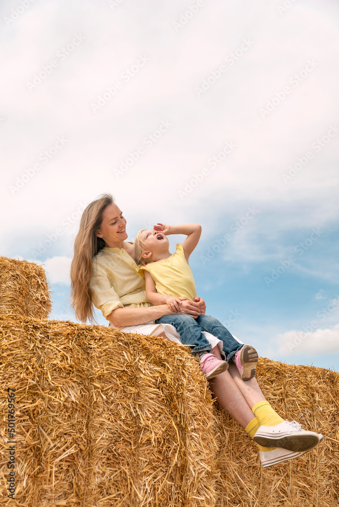 Young mom and little daughter have fun on the farm playing on the haystack. Countryside summer weekends. Young mom and little daughter have fun on the farm playing on the haystack. Countryside summer weekends.