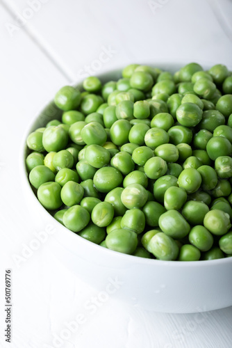Green peas in white bowl with fresh pods on the wooden table. 