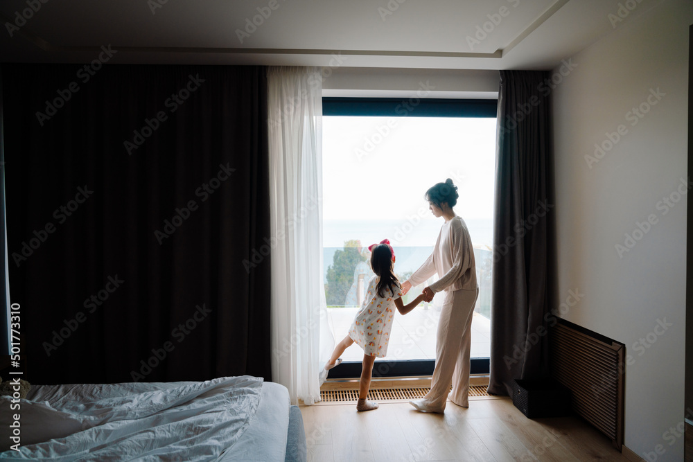Asian woman and her daughter looking out window while together