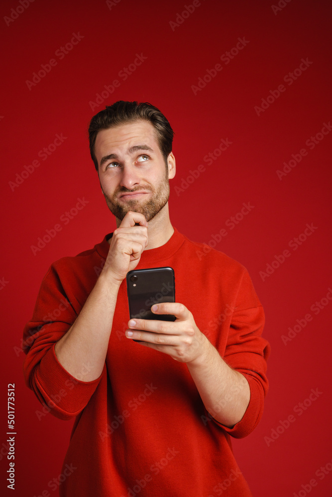 Young perplexed man looking at camera and using cellphone Young perplexed man looking at camera and using cellphone
